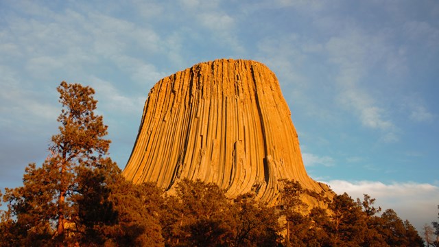 A scenic view of Devils Tower National Monument under a clear blue sky, highlighting its unique rock formations and surrounding landscape